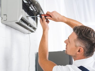 handsome adult man repairing air conditioner with screwdriver